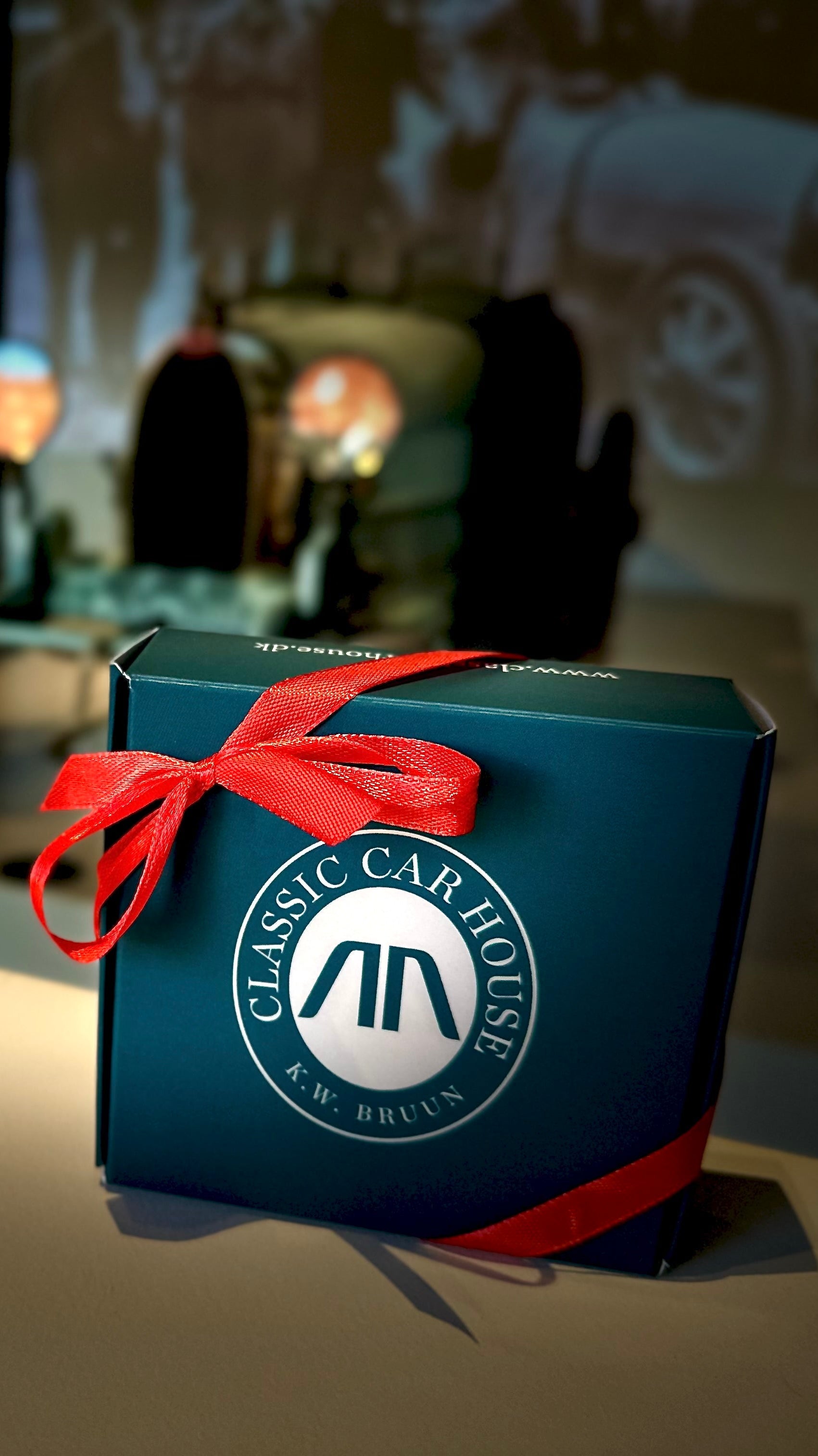 Gift box with Classic Car House logo and red ribbon and the blue box standing Bugatti special exhibition in a cozy lighting.